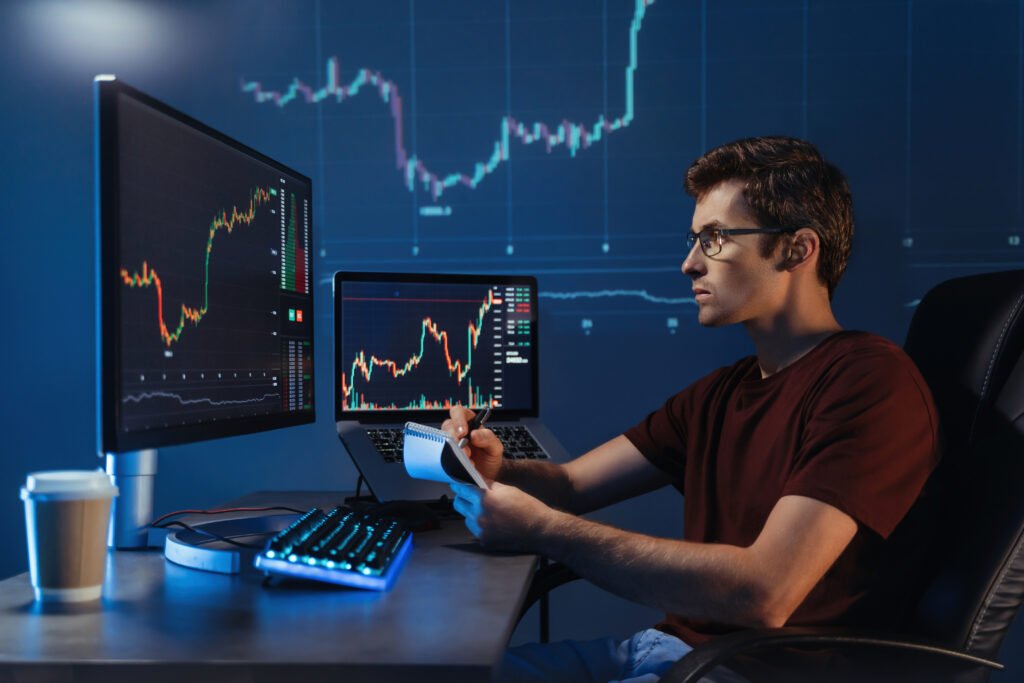 Crypto broker sitting at his workplace, looking at computer monitor, checking candlestick chart